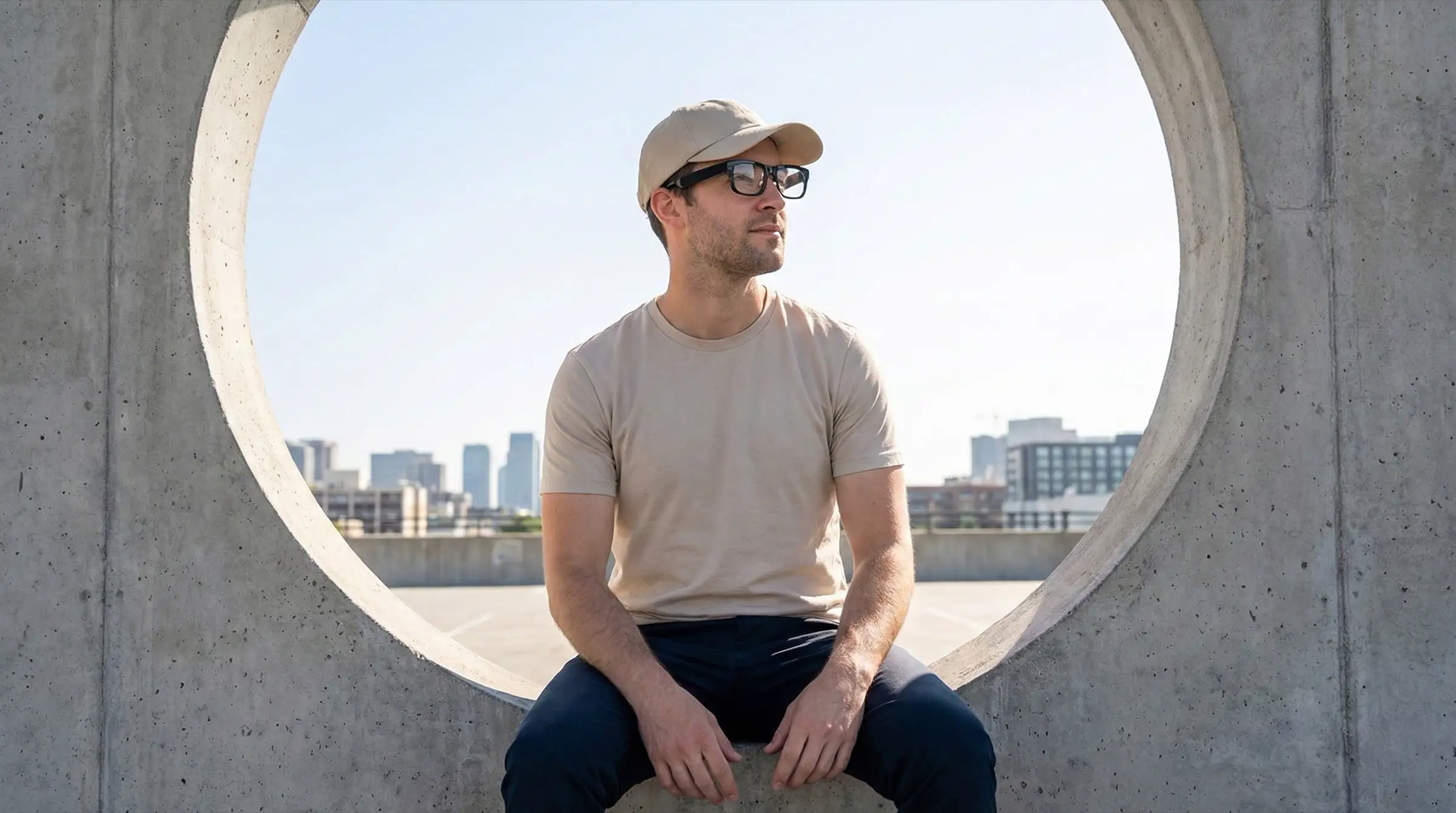 A traveller in a cap and the glasses sits inside a concrete ring above a city skyline.