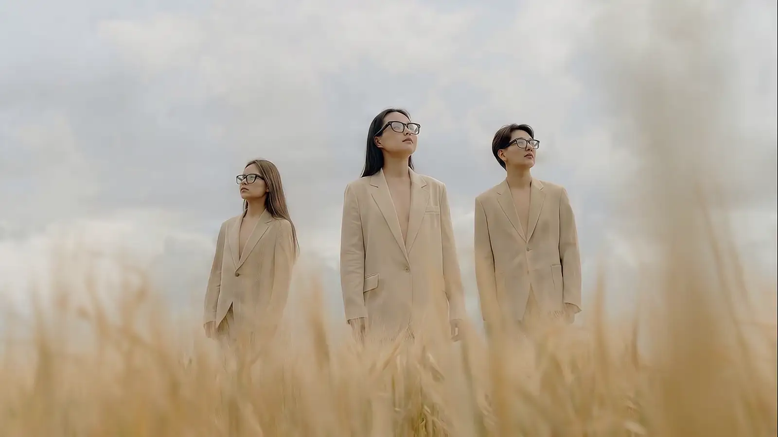 Three people in beige suits walk through a wheat field, wearing the glasses.